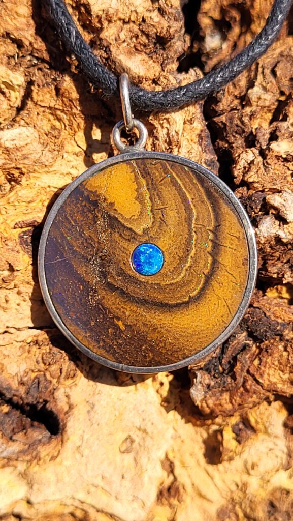 Pendentif rond en opale boulder d'Australie, avec une opale cristal bleu en son centre. Le bijou est en argent 925.